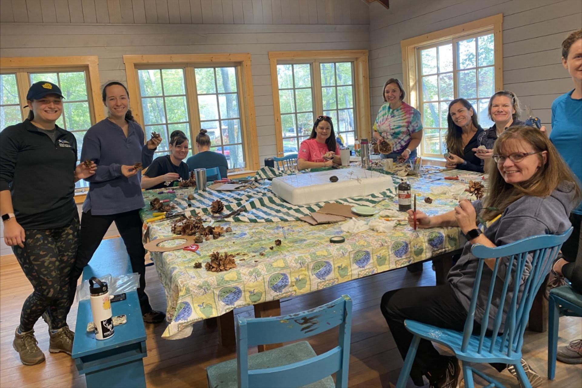 A group of 10 women working on a craft around a large table at Camp Newaygo