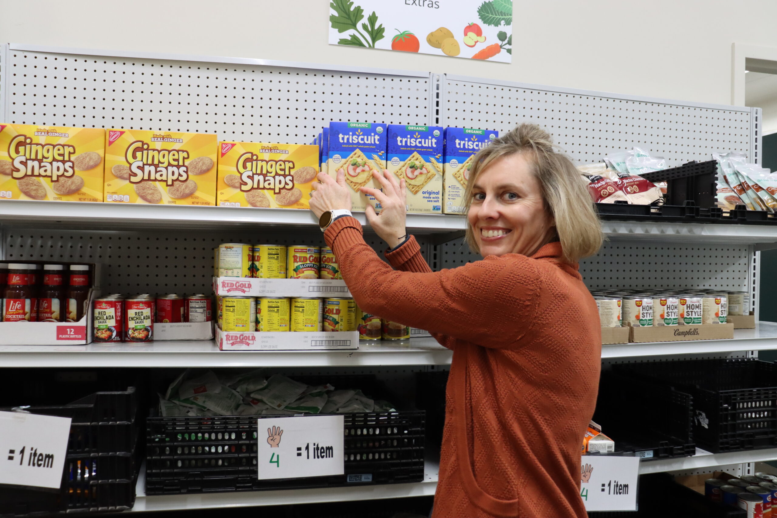 Female volunteer, in an orange sweater, stocking shelves in the TrueNorth Food Center