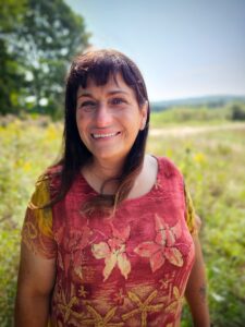 woman in a pink shirt smiling in front of a field for Homeless Awareness Month