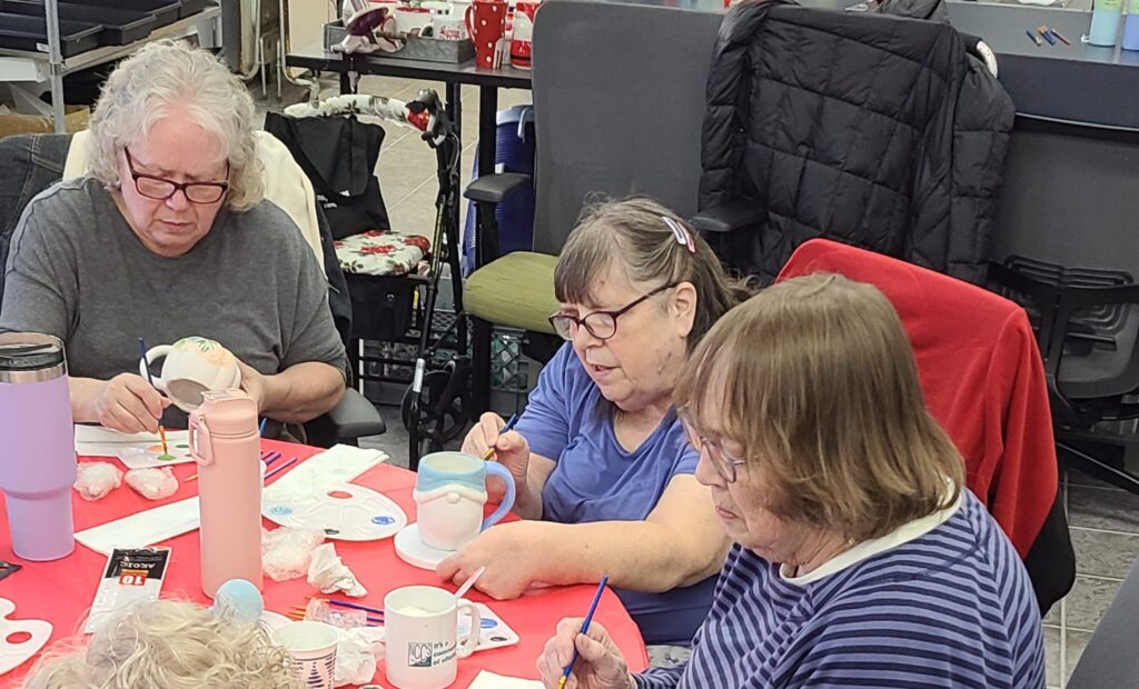 Three ladies painting mugs at Community Connections.