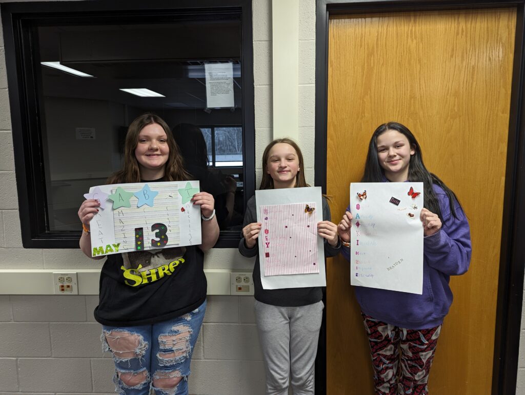 Three middle school girls holding up posters they made at TrueBlue Academy.